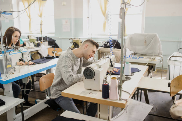 工場のミシンで縫っている青年や他のストレスの縫製の写真を閉じます - 写真・画像