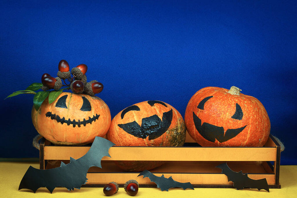 Halloween kreatív sütőtök vicces mosollyal arcok és papírdenevérek kék sárga háttér. Kiváló minőségű fénykép - Fotó, kép