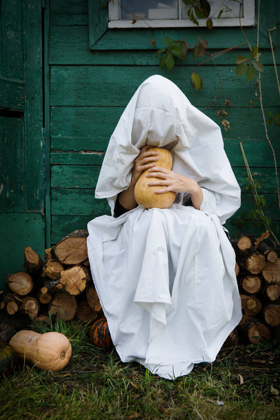 Happy Halloween! Woman in ghost costume with pumpkin in the garden - Фото, зображення