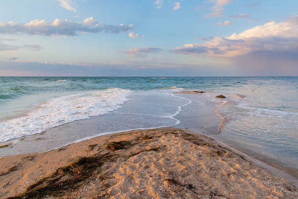 Bord de mer au coucher du soleil, le sable est lavé de deux côtés par les vagues, les nuages dans le ciel - Photo, image