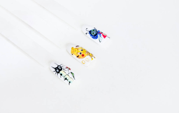 muestras de uñas con diseño de manicura con oruga, tetera y mosca dispuestos en una línea en el fondo blanco - Foto, imagen