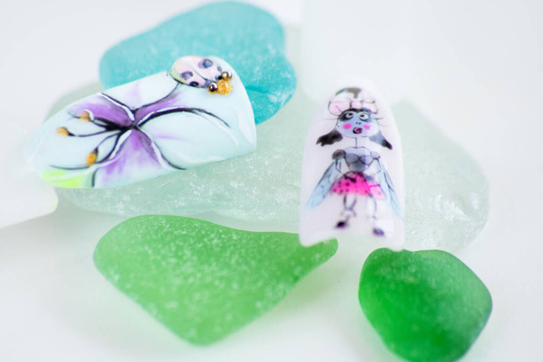 muestras de uñas con una mosca en un vestido y mariquita, diseño de manicura. en piezas del vidrio de color en el fondo blanco - Foto, Imagen