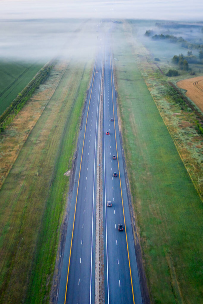 Autópálya a mezőn, ködben, erdővel körülvéve. Köd borította út légi rálátása. - Fotó, kép