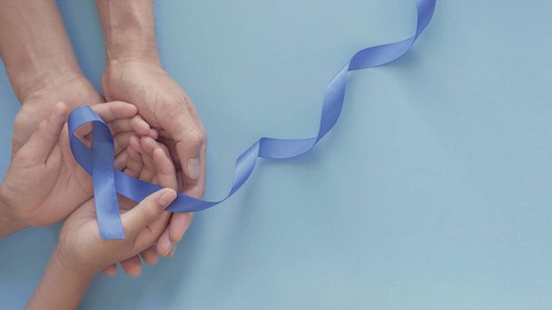 adult and child hands holding blue ribbon on blue background, Prostate Cancer Awareness - Фото, изображение