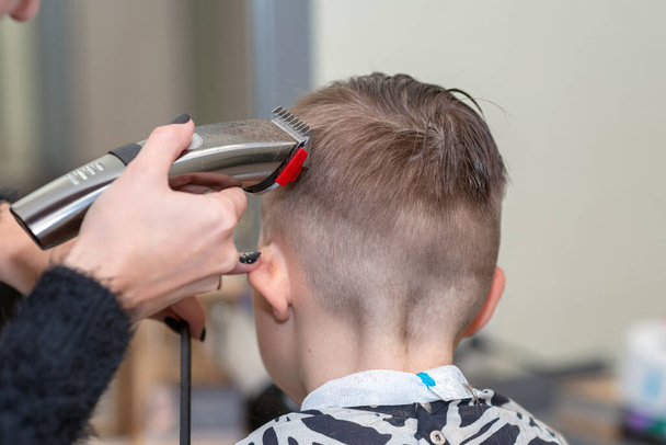 Vue de dos Happy boy est assis dans le salon de coiffure avec les cheveux mouillés et lui coupe les cheveux. - Photo, image