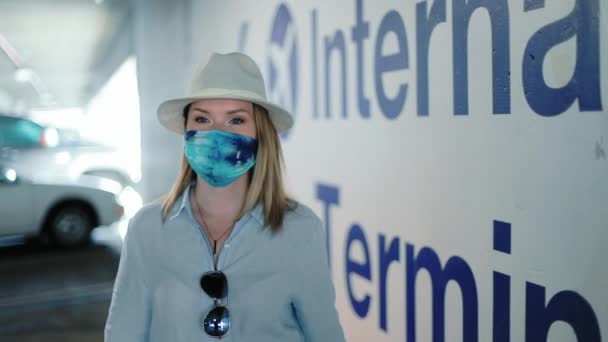 Viajante elegante em máscara colorida está no aeroporto estacionamento rumo a portões - Filmagem, Vídeo