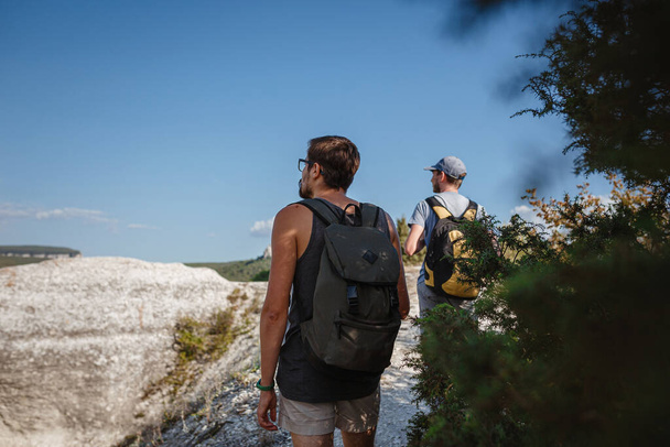 Due uomini che camminano su pendio roccioso portando zaini utilizzando bastoni da trekking. Montagne valle Vista accanto alla gente. estate viaggio nella natura. Escursionista sullo sfondo. - Foto, immagini