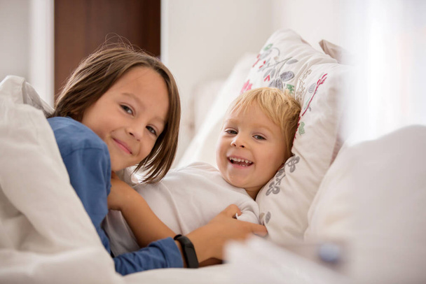 Two sweet children, boy brothers, lying in bed together, talking and smiling - Foto, Bild