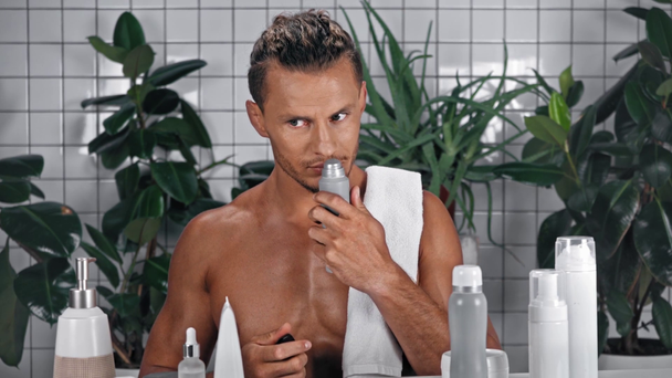 Άνδρας με πετσέτα μυρίζοντας προϊόντα περιποίησης στο μπάνιο - Πλάνα, βίντεο