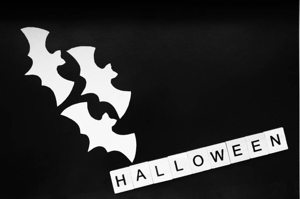 Белые летучие мыши лежат на черном фоне. Слово Хэллоуин из деревянных блоков с буквами - Фото, изображение