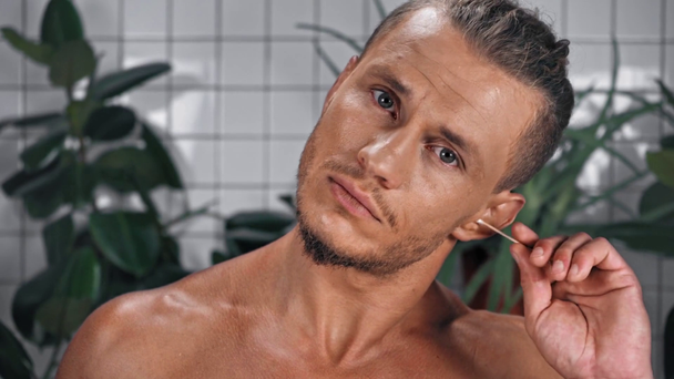 Retrato del hombre mirando a la cámara y usando el palo de oído en el baño - Metraje, vídeo