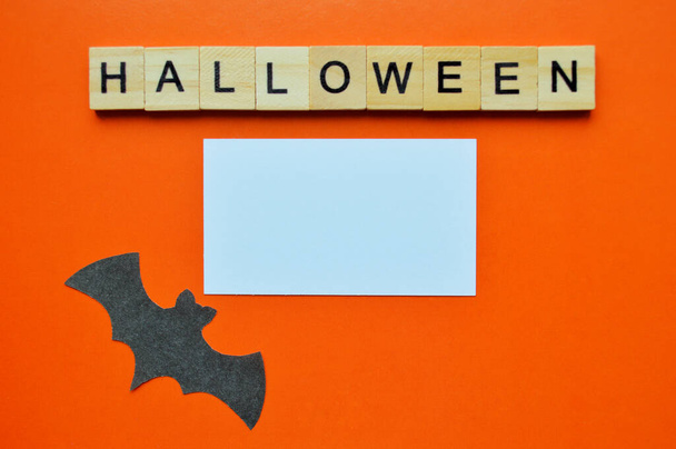 Black paper bat lies on orange background with white mockup. Word halloween of wooden blocks with letters - Foto, Bild