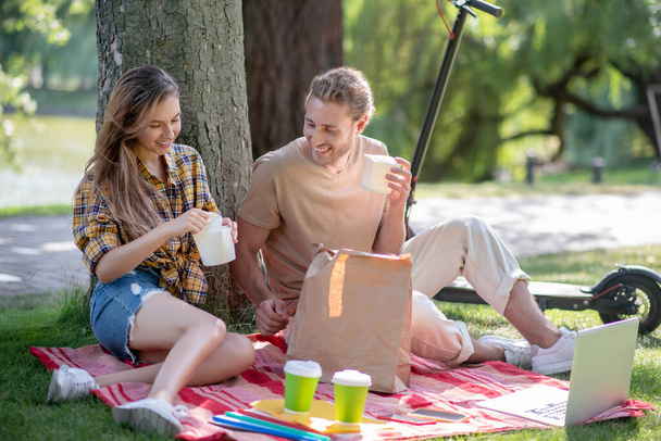 Young couple resting in the park and having lunch under the tree - Foto, imagen