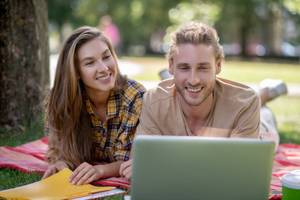 Young couple lying on the grass and watching something on a laptop - Foto, Imagem
