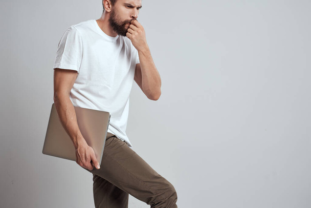 Um homem com um laptop em suas mãos em um fundo leve em uma camiseta branca emoções luz de fundo novas tecnologias - Foto, Imagem