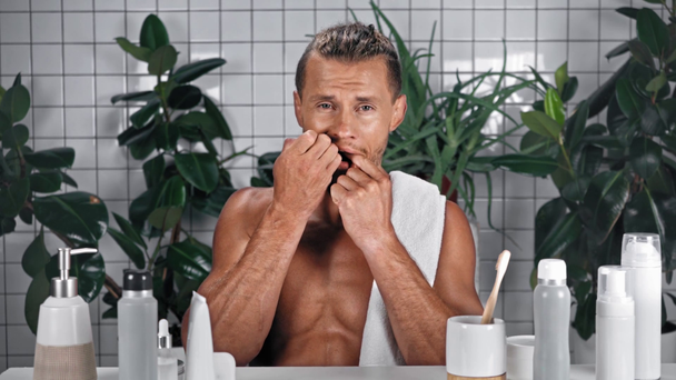 Uomo utilizzando filo interdentale e mostrando i denti in bagno - Filmati, video