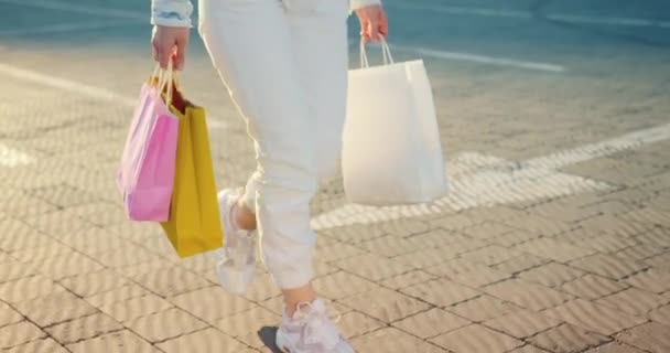 Zbliżenie dziewczęcych stóp spacerujących po parkingu. Ma w rękach torby na zakupy. 4K - Materiał filmowy, wideo