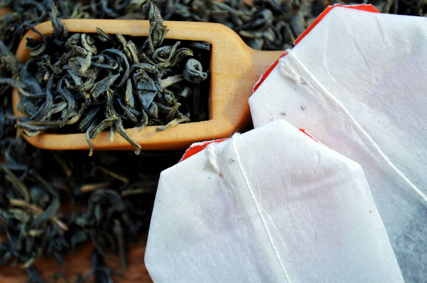 Des sachets de thé et une cuillère en bois reposent sur un tas de thé sur un fond en bois - Photo, image
