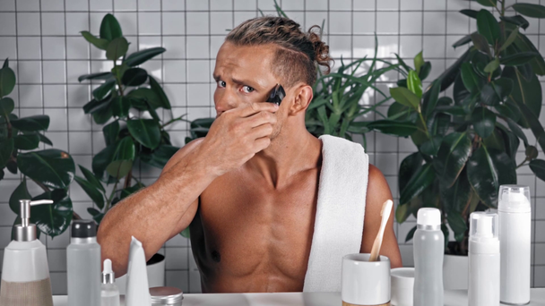 Man looking at camera and shaving whiskers with electric razor - Footage, Video