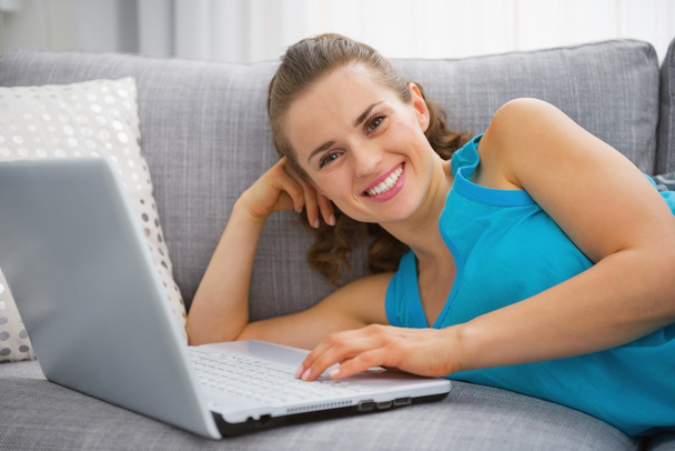 Smiling young woman laying on sofa with laptop - Photo, Image