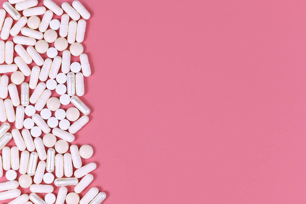 White medical capsule pills on left side of pink background with blank copy space - Foto, immagini