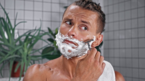 Hombre con toalla de afeitar con afeitadora de seguridad en el baño - Imágenes, Vídeo