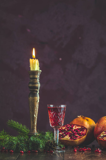 Greeting food Christmas and New Year composition. Vintage glass of pomegranate drink surrounded pine branches and festive candles, dark background - Photo, Image