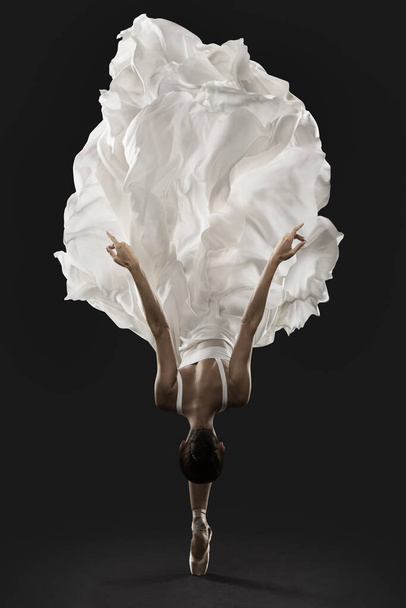 Ballerina Graceful Jump in White Silk Dress, Ballet Dancer Pointe Shoes in Fluttering Cloth, Black Backgroun - Foto, imagen