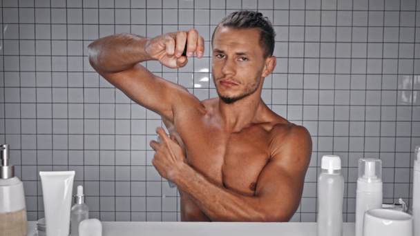 Uomo guardando la fotocamera e spruzzando deodorante in bagno - Filmati, video