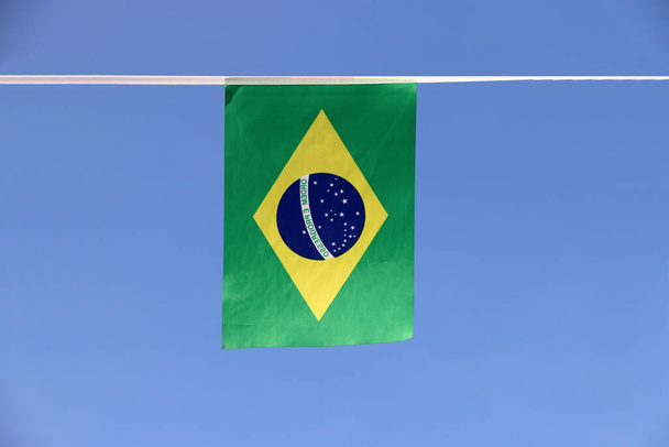 Mini bandiera ferroviaria in tessuto del Brasile, un disco blu raffigurante un cielo stellato con il motto nazionale Ordine e progresso, all'interno di un rombo giallo, su un campo verde. E 'appeso sul panno corda su sfondo cielo blu. - Foto, immagini