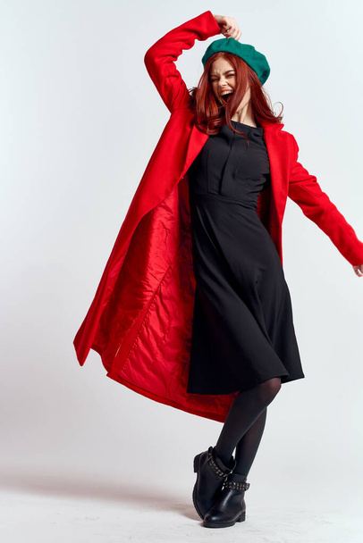эмоциональная женщина в красном пальто и в шляпе в полный рост на светлом фоне черный сапоги позируют модель - Фото, изображение