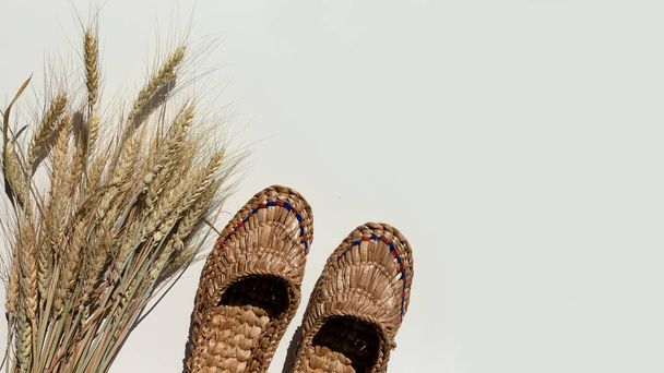 Pair of old bast shoes and a sheaf of wheat on a light background. Copy space. - Photo, Image