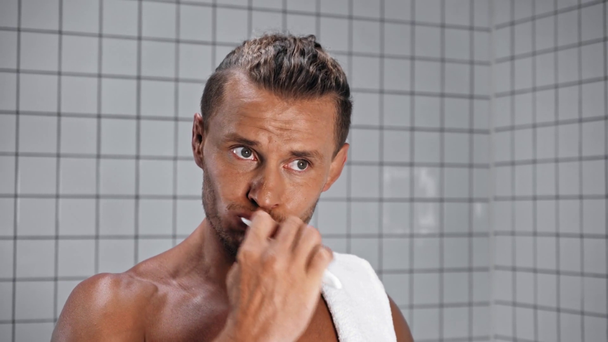 Άντρας με πετσέτα βουρτσίζει τα δόντια με πλακάκια στο παρασκήνιο - Πλάνα, βίντεο