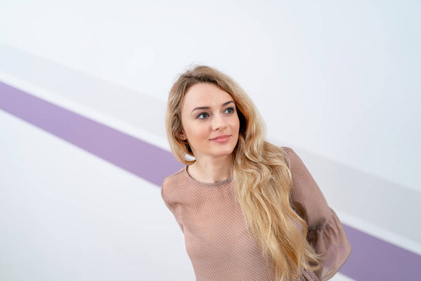 Beautiful blonde girl with long hair posing near wall in beige shirt. half waist portrait. - Фото, зображення