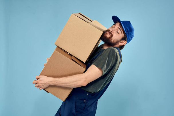 Man in working uniform with boxes in hands delivery service blue background - Photo, Image