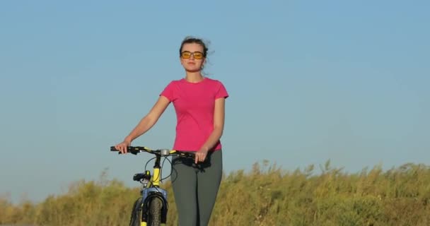 Rowerzysta spacerujący z rowerem po drodze w żółtych okularach - Materiał filmowy, wideo