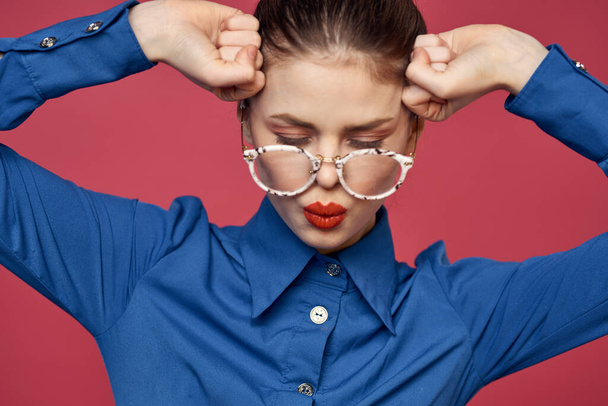 Retrato de una mujer en gafas y en una camisa azul labios rojos fondo rosa modelo - Foto, Imagen