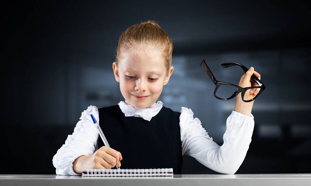Sonriente niña en ropa de escuela haciendo la tarea - Foto, imagen