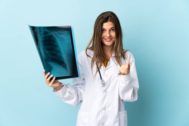 Junge Ärztin hält Röntgenbild über isoliertem Hintergrund und macht Geld-Geste - Foto, Bild