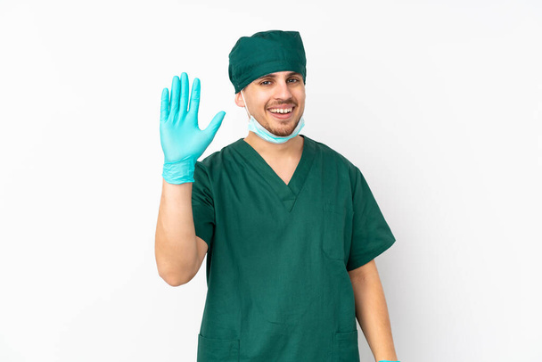幸せな表情で手で隔離された白い背景の塩漬けに隔離された緑の制服を着た外科医 - 写真・画像