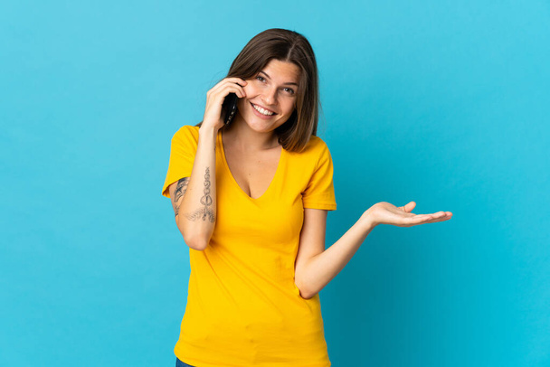 Junge slowakische Frau isoliert auf blauem Hintergrund hält ein Gespräch mit dem Handy mit jemandem - Foto, Bild