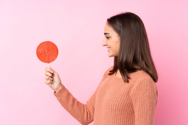Young girl holding a lollipop over pink background with happy expression - Фото, зображення