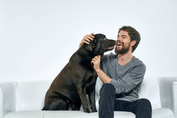 Homme avec un chien de compagnie sur le canapé amusement amis émotions salle de lumière - Photo, image