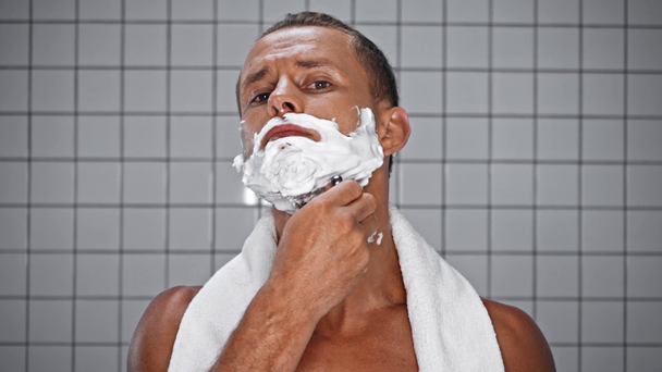 Portret mężczyzny z goleniem ręcznikiem z maszynką do golenia w łazience - Materiał filmowy, wideo