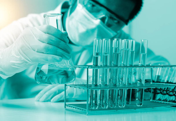 Tutkija, jolla on kädessään pullo, joka kaataa näytettä koeputkeen ja tieteellisiin kokeisiin, Laboratorion lasitavarat, jotka sisältävät kemiallista nestettä,  - Valokuva, kuva