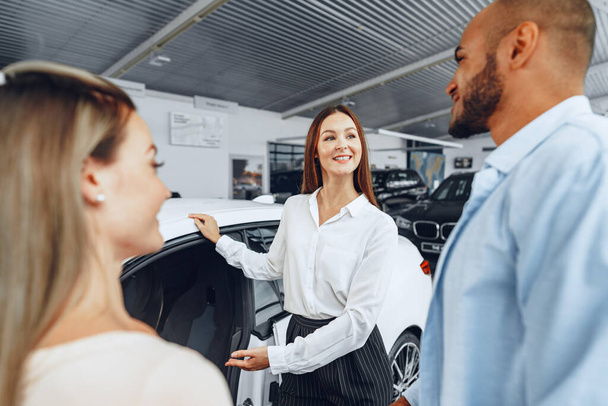 Woman car dealer explaining to buyers features of their new car - Fotó, kép