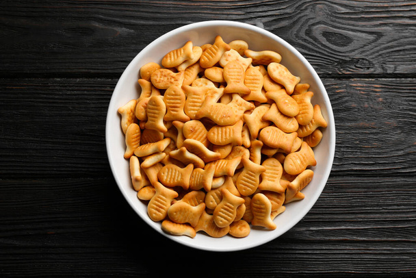 Delicious goldfish crackers in bowl on black wooden table, top view - Foto, immagini