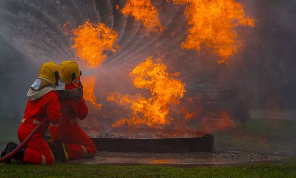 Dois bravos bombeiros usando extintor e água da mangueira para combate a incêndios, Bombeiro pulverizando água de alta pressão para disparar, Bombeiro treinando com chamas perigosas, Copiar espaço-imagem - Foto, Imagem