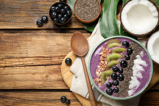 Delicious acai smoothie and fruits in bowl served on wooden table, flat lay. Space for text - Foto, Imagem