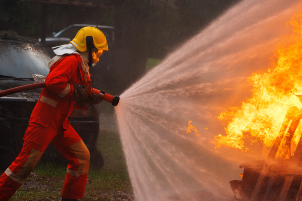 Urhea palomies, joka käyttää sammutinta ja vettä letkusta palontorjuntaan, palomies ruiskuttaa korkeapainevettä tuleen, palomiehen koulutus vaarallisilla liekeillä, Kopioi tilaa-kuva - Valokuva, kuva